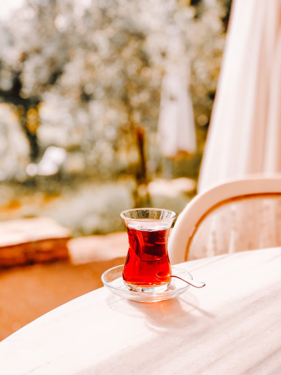 Traditional Turkish tea in a glass with spoon on a marble table, blurred garden background.