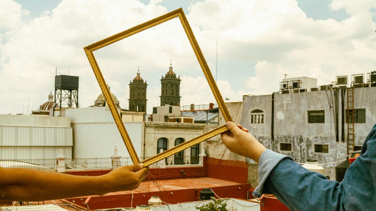 Hands holding a frame with Puebla cityscape including church towers, capturing a unique perspective.