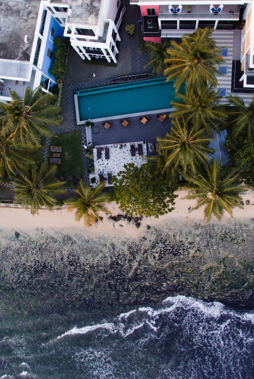 A breathtaking aerial view of a beachfront resort with palm trees and a pool near the ocean.