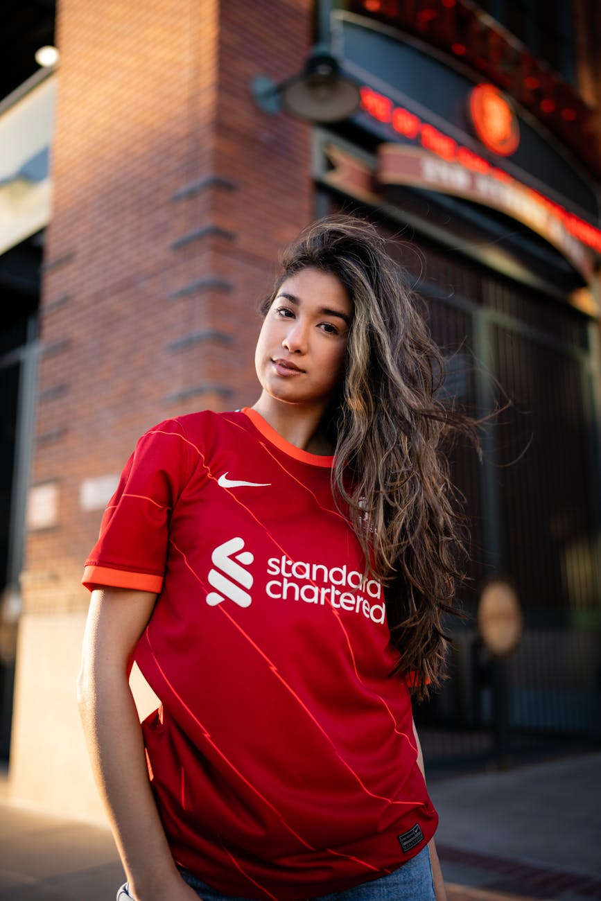 Portrait of a woman wearing a Liverpool FC jersey, posing outdoors in an urban environment.