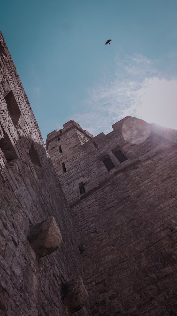 Low angle view of Caernarfon Castle's stone tower against a bright blue sky in Wales, UK.