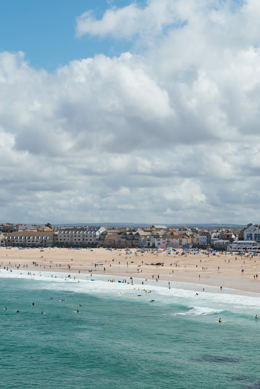 A vibrant summer day at St Ives beach in England, capturing people enjoying the sea and sand under a cloudy sky.
