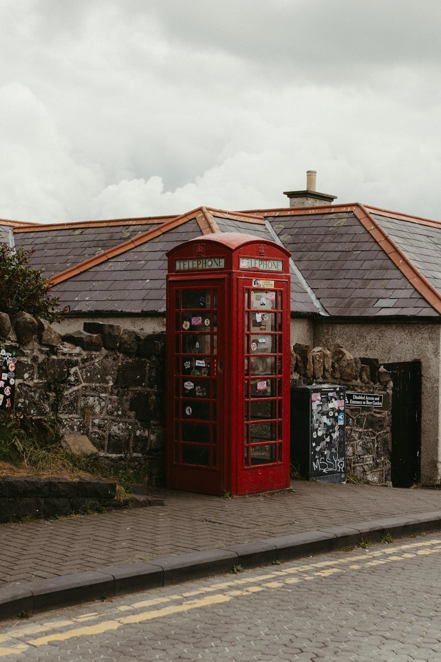 Classic red phone booth beside stone wall in Northern Ireland, showcasing local charm.