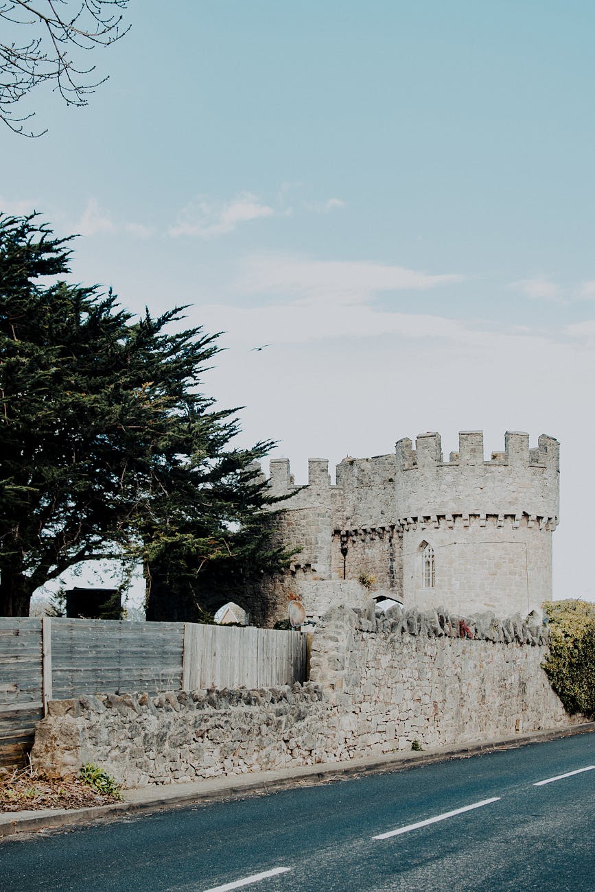 A scenic view of a historic castle by the roadside in Abergele, Wales against a clear blue sky.