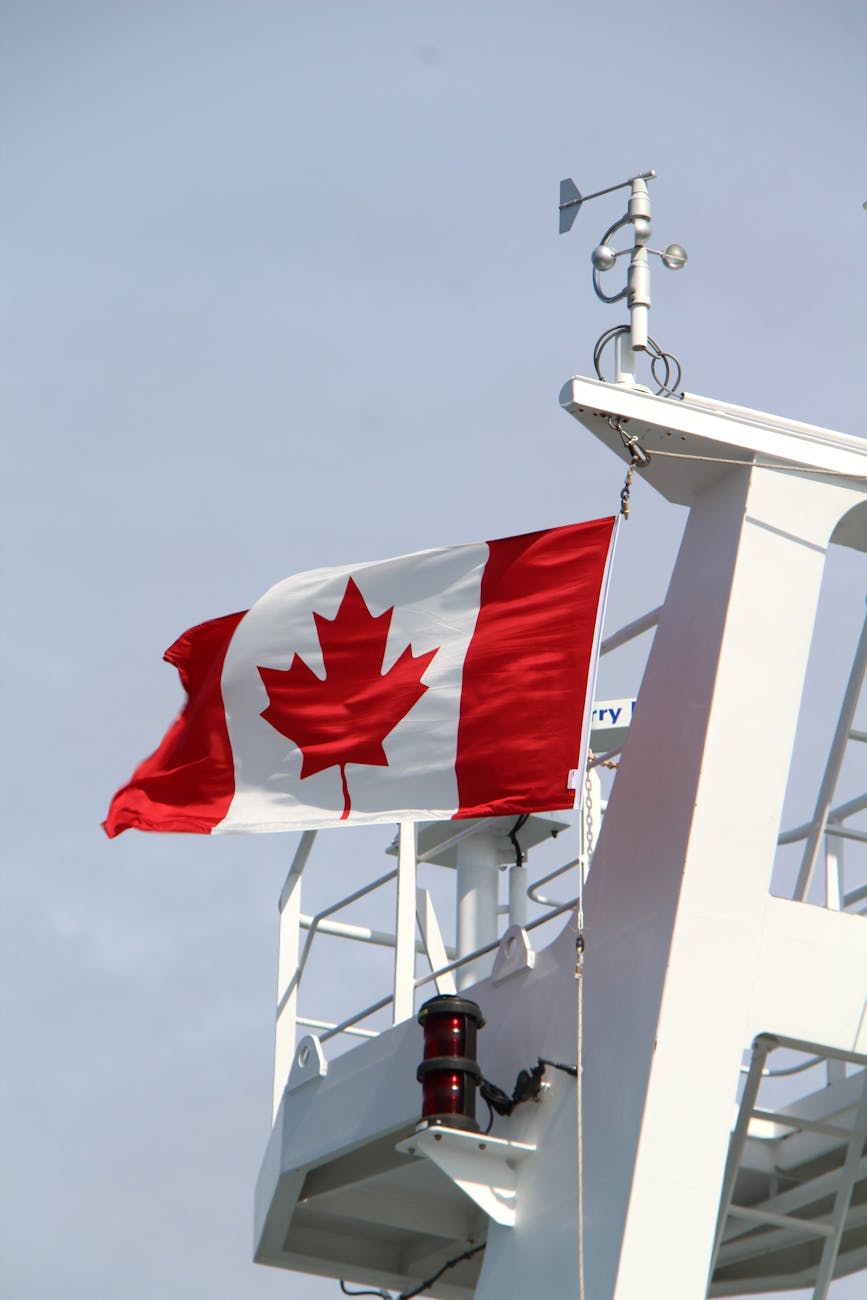 A Canadian flag waves on a ship mast against a clear sky, symbolizing national pride.