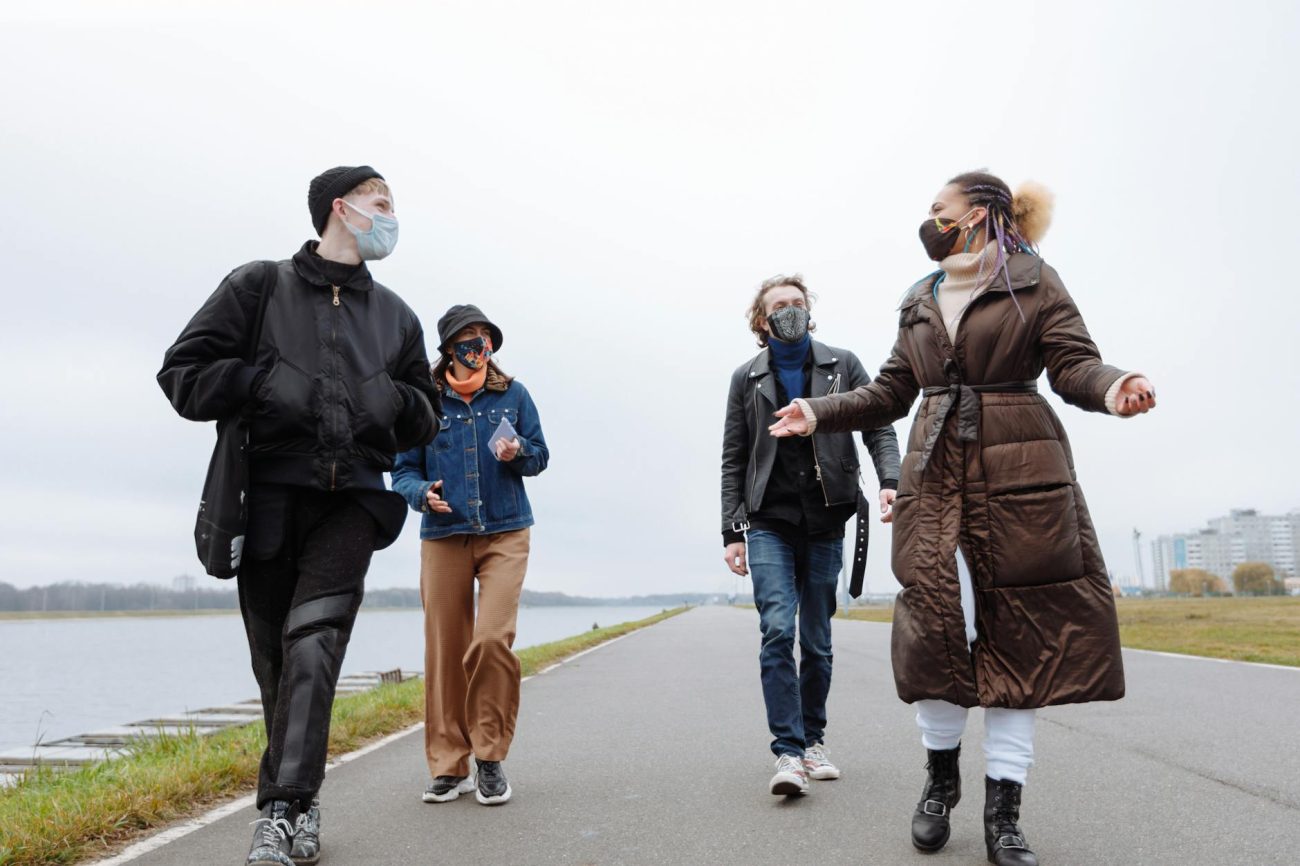 A diverse group of friends walking along a riverside path wearing face masks.