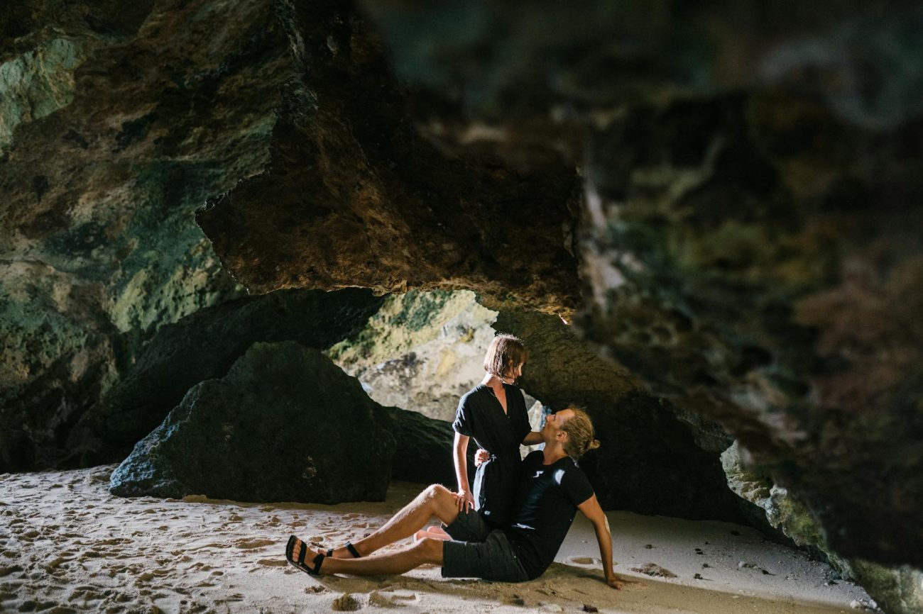 A couple shares a romantic moment inside a secluded beach cave, surrounded by natural beauty.
