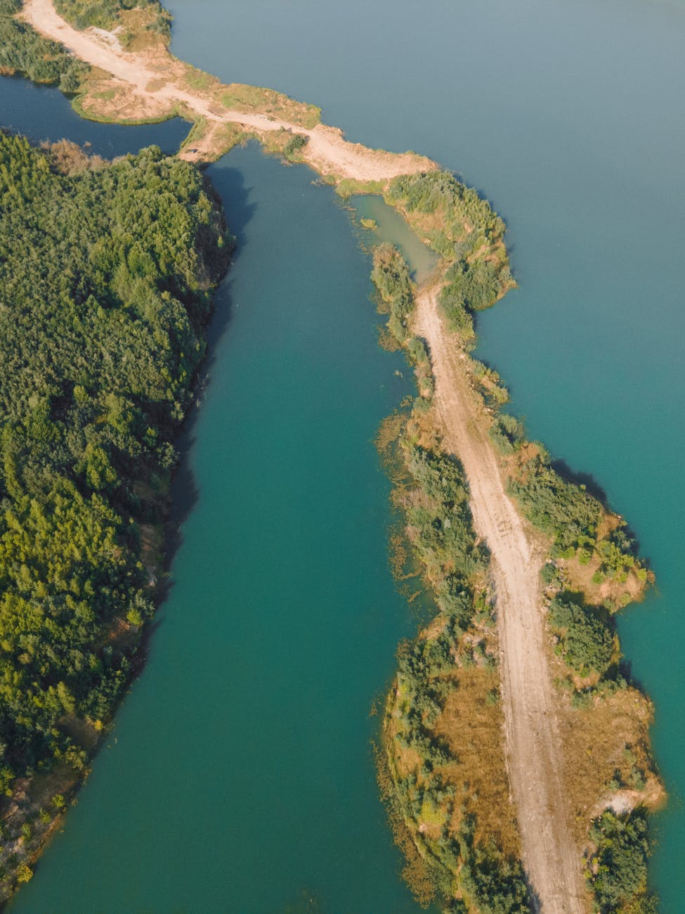 Stunning aerial photo showing a rural dirt path cutting through lush greenery and crystal-clear water.