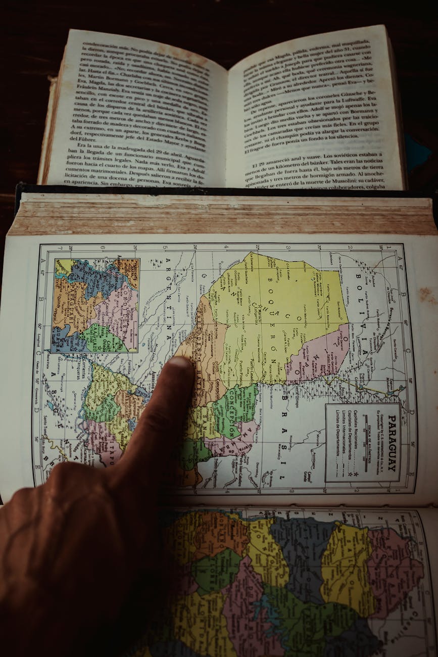 Finger pointing to a Paraguay map in an atlas with an open book, ideal for travel and education themes.